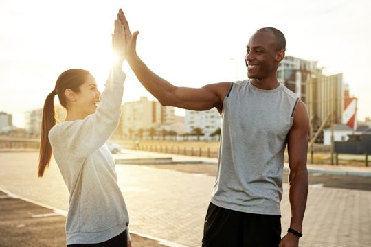 Shot of a sporty young man and woman giving each other a high five while exercising outdoors